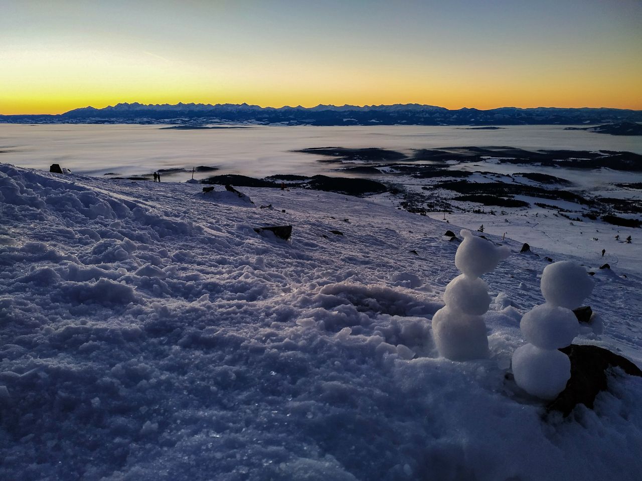 Trzy małe bałwany ulepione na szczycie Babiej Góry o świcie, w tle Tatry nad morzem chmur