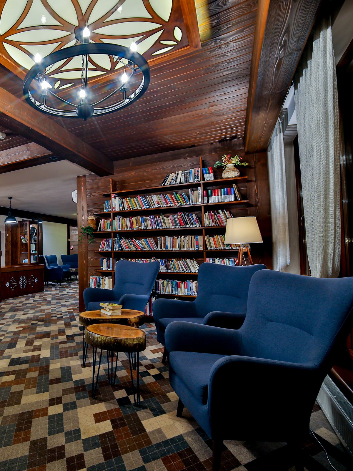 Biblioteczka w holu Hotelu Jawor — regały z książkami, lampa i granatowe fotele przy stolikach z pieńków