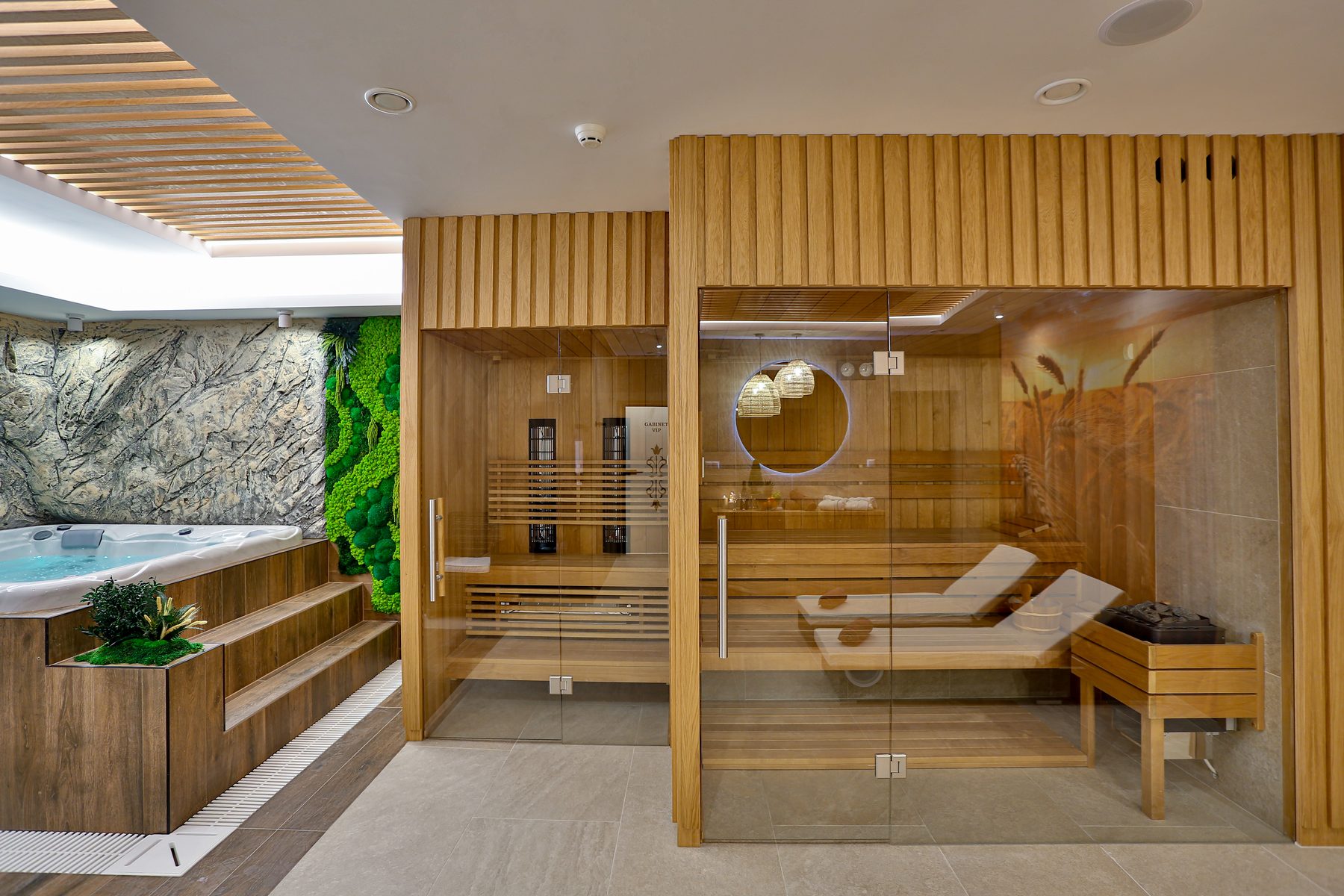 Gabinet VIP w szerokim kadrze — jacuzzi, przeszklona sauna i ściana skalna
