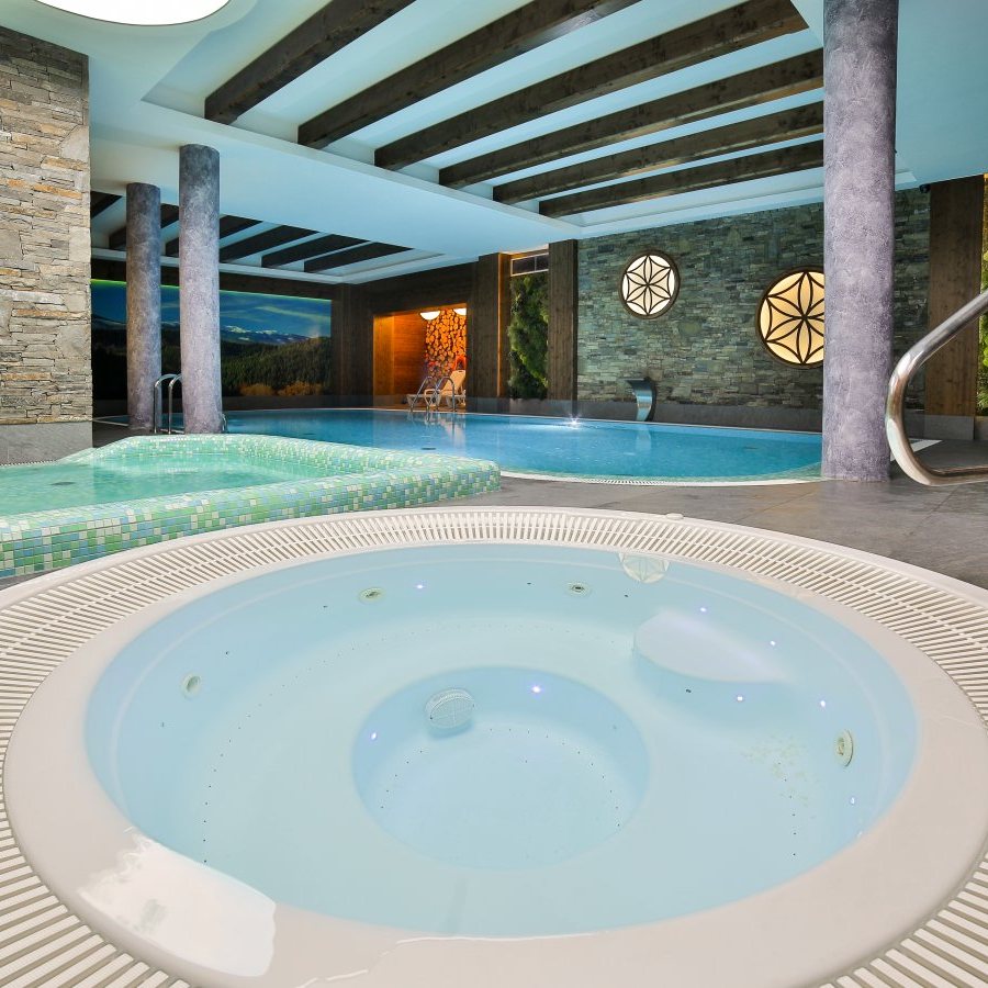 Jacuzzi wewnętrzne przy basenie krytym, w tle brodzik i niecka basenu