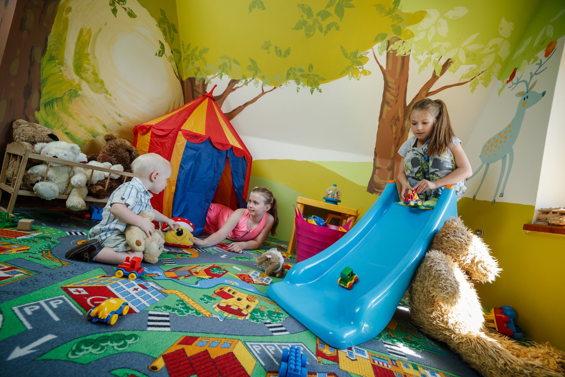 Dzieci bawiące się w kidsroomie Hotelu Jawor — zjeżdżalnia, namiot tipi i dywan z drogami