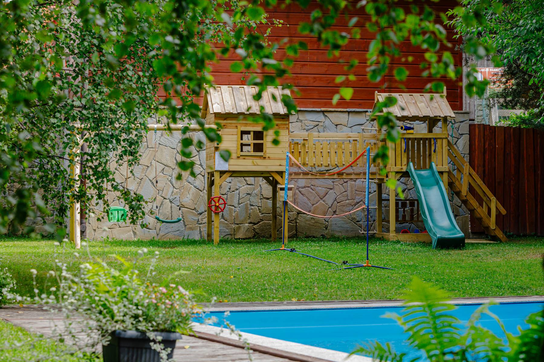 Plac zabaw przy Hotelu Jawor — drewniany domek ze zjeżdżalnią obok basenu letniego