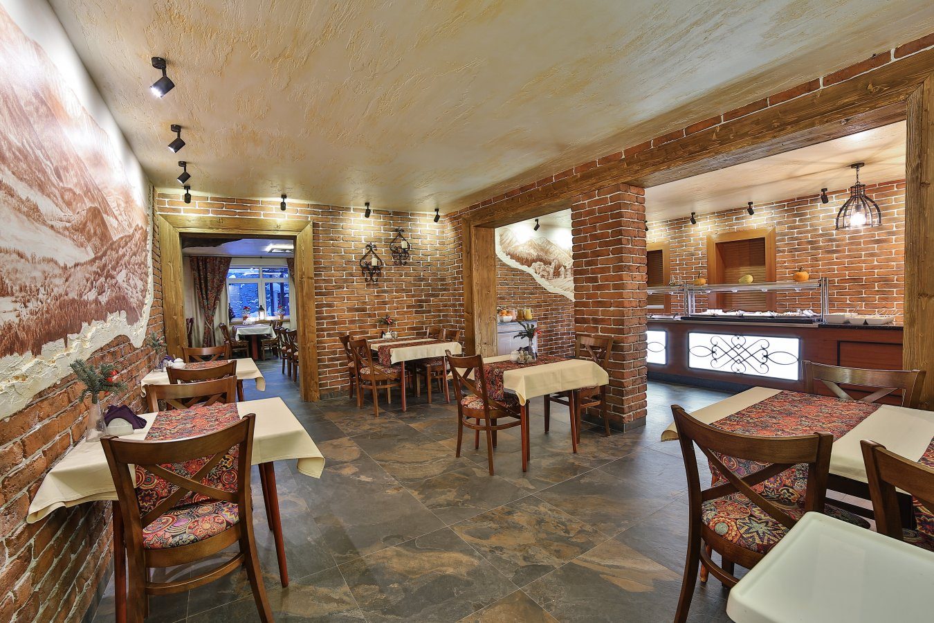 Sala restauracji z ceglaną ścianą i malowaną panoramą, w głębi bufet