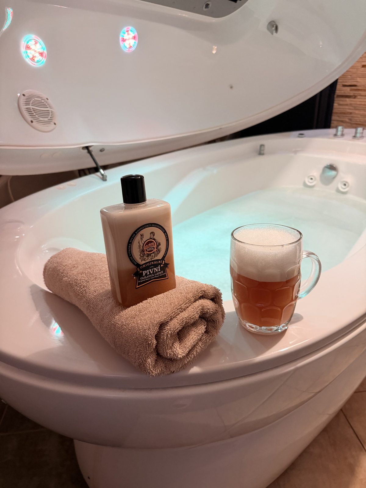 Kąpiel piwna w kapsule SPA Hotelu Jawor — kosmetyk do kąpieli piwnej, zwinięty ręcznik i kufel piwa na brzegu wanny