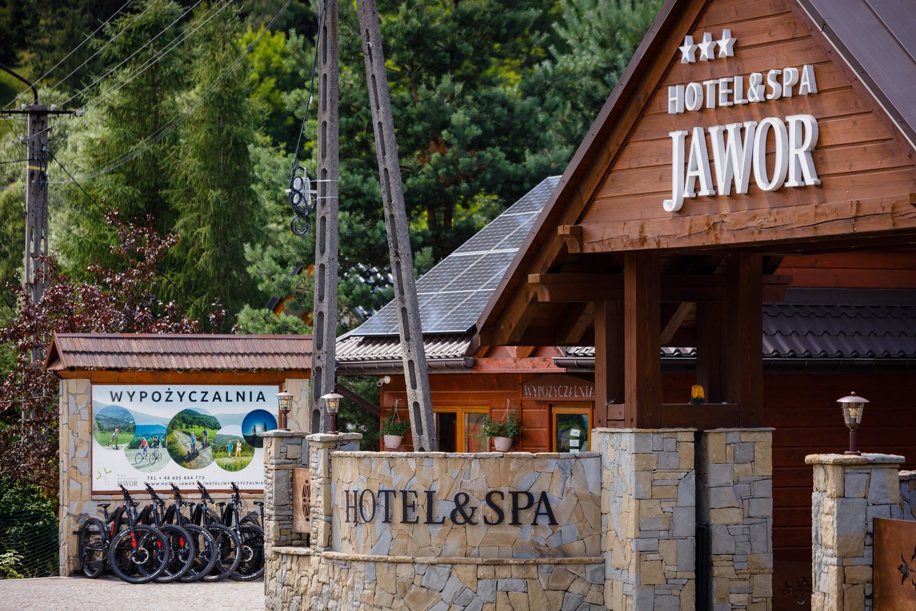 Brama wjazdowa z szyldem Hotelu & SPA Jawor i rowery elektryczne przed Wypożyczalnią Jawor