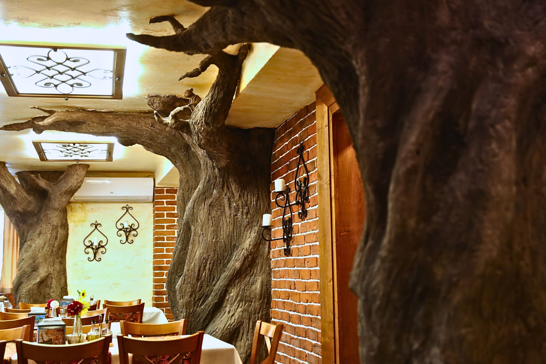 Sala restauracji, w której strop podpierają pnie drzew, i kute świeczniki na ceglanej ścianie