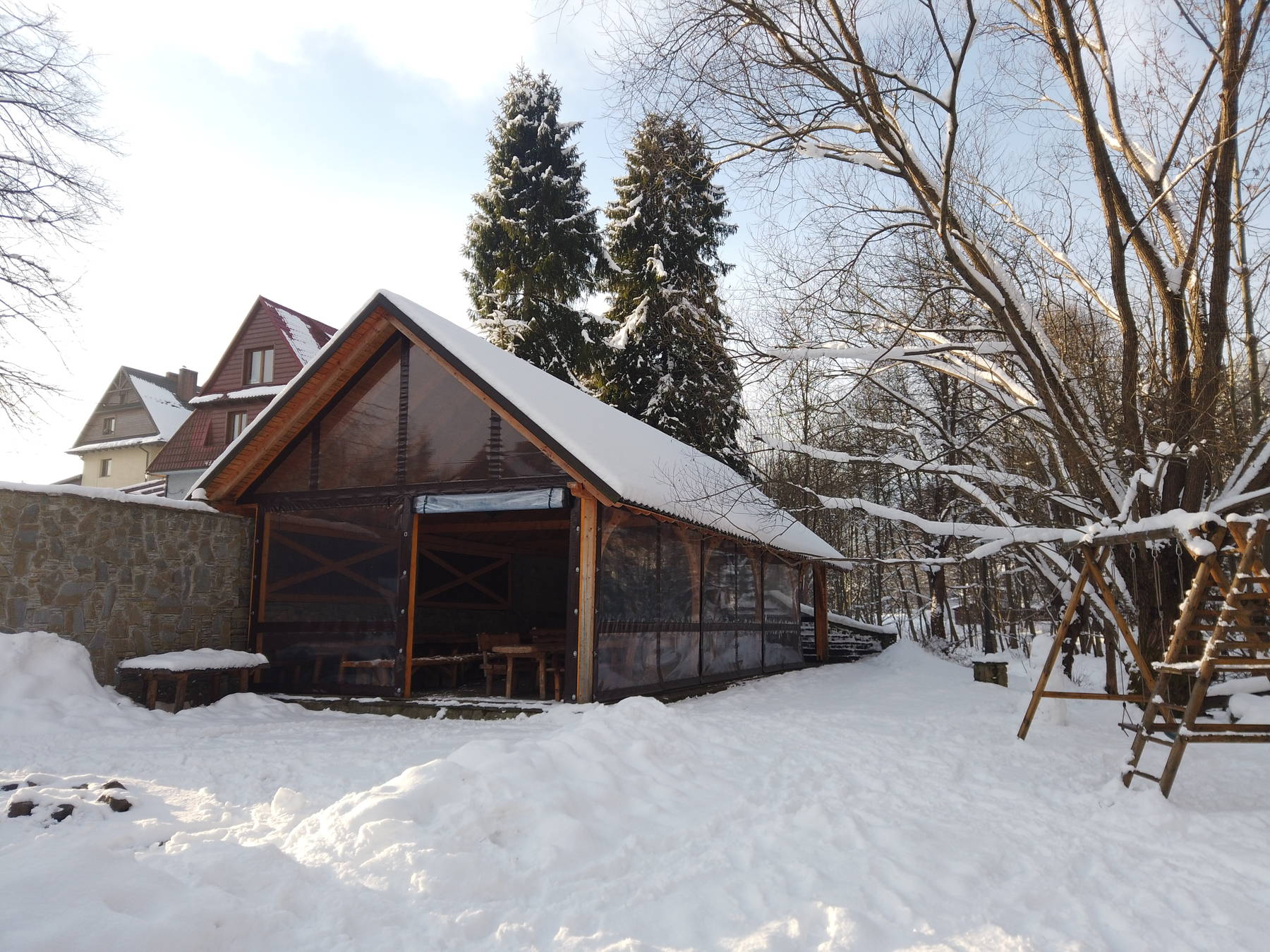 Wiata grillowa nad potokiem zimą — przezroczyste ściany boczne i śnieg na dachu