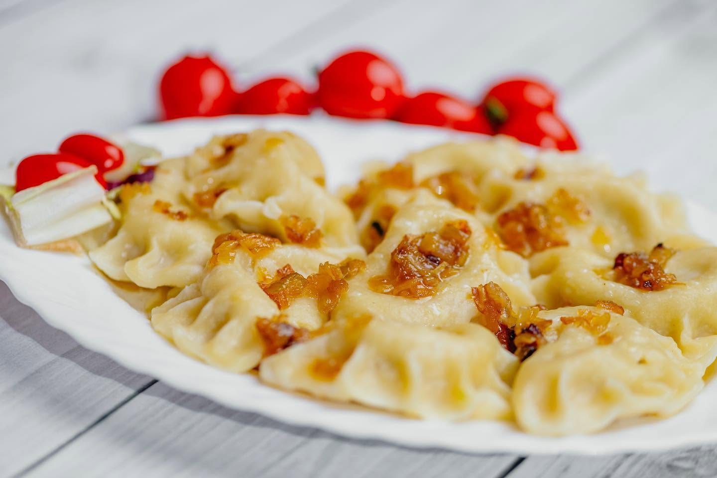Pierogi polane podsmażoną cebulką na białym talerzu, obok pomidorki koktajlowe — danie z karty restauracji Hotelu Jawor